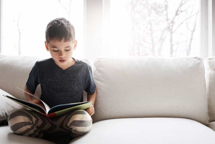 Shot of an adorable little boy reading a book while relaxing on the sofa at home