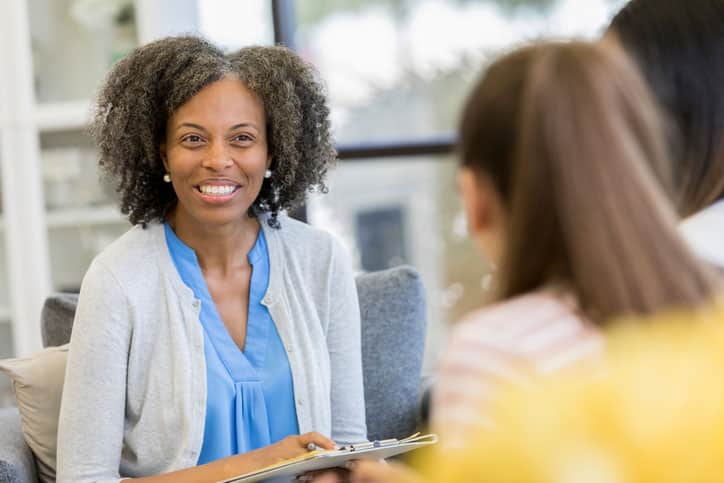 Encouraging mature high school guidance counselor smiles as she discusses education options with female high school students.