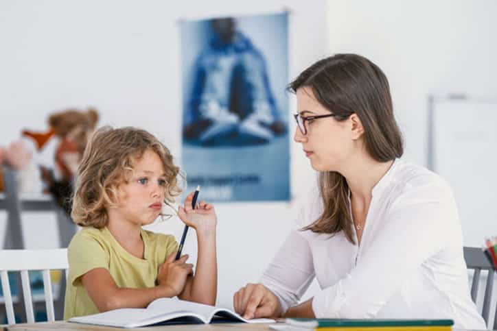 A young female tutor having a lesson with an absentminded child with concentration issues.