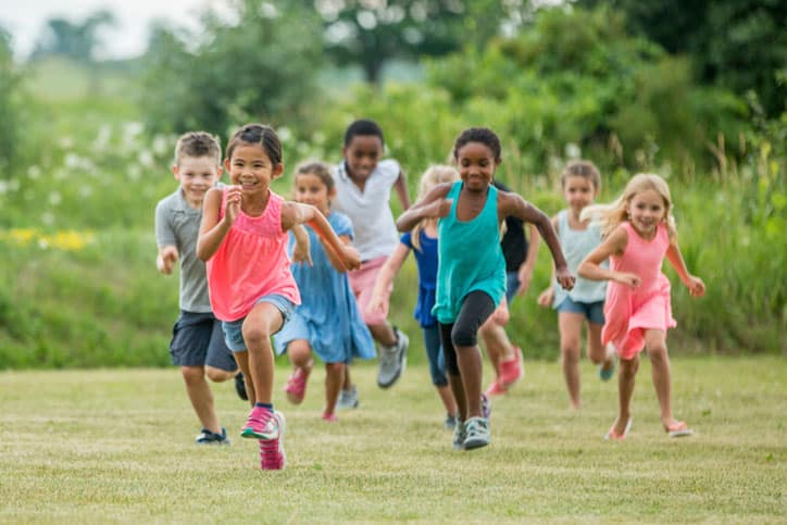 A multi-ethnic group of elementary age children are playing together outside at recess. They are chasing each other and are playing tag.