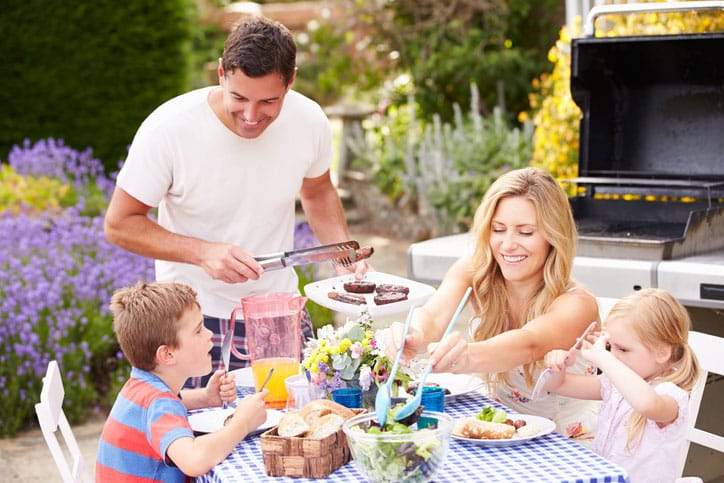 Family Enjoying Outdoor Barbeque In Garden On Sunny Day